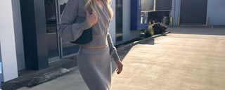 Woman in a gray outfit walking outdoors near a building.