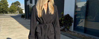 Woman wearing a black tie blazer standing outside a building with trees in the background