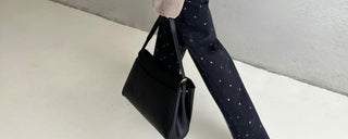 Woman holding a black handbag in studd jeans with a neutral background