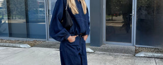 Woman wearing a blue denim outfit standing outside a building with glass doors.
