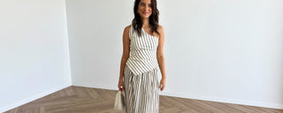 Woman in a striped top and skirt set standing in a minimalistic room with white walls and wooden floor.