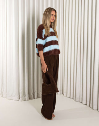 Woman wearing a brown and blue striped sweater with wide-leg pants against a white curtain background