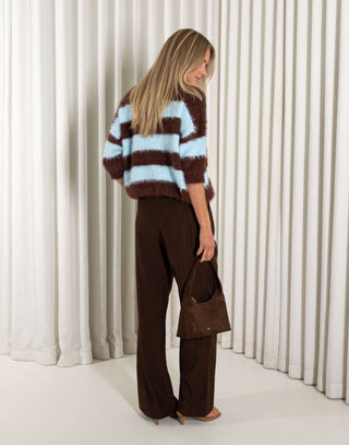 Woman wearing a brown and blue striped sweater with wide-leg pants against a white curtain background