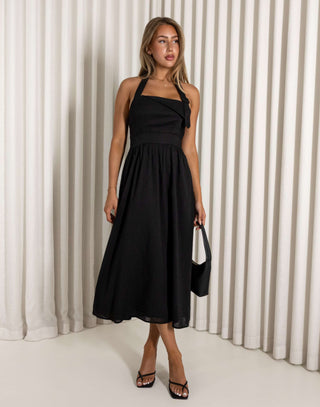 Woman wearing a black halter neck dress against a white curtain background Black halter neck midi dress with flared skirt
