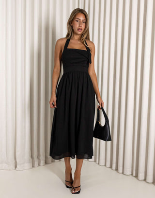Woman wearing a black halter neck dress against a white curtain background Black halter neck midi dress with flared skirt