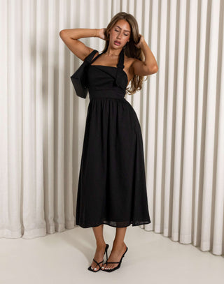 Woman wearing a black halter neck dress against a white curtain background Black halter neck midi dress with flared skirt