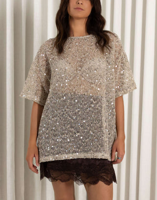 Woman wearing a sequin top with a plain background Beige knit top with scattered sequin detailing and short sleeves
