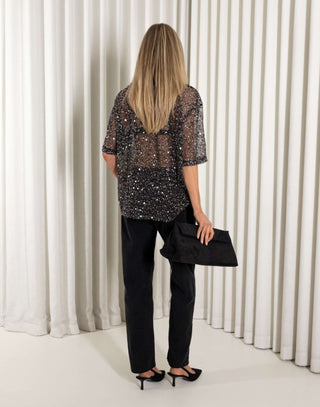 Woman wearing a sequin top and black pants against a white curtain background