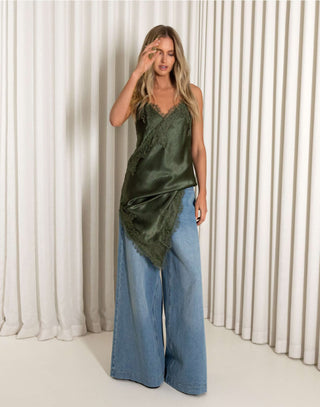 Woman wearing a green satin top and blue jeans against a white curtain background
