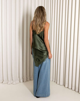 Woman wearing a green satin top and blue jeans against a white curtain background