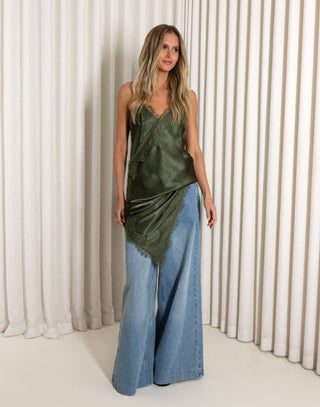 Woman wearing a green satin top and blue jeans against a white curtain background