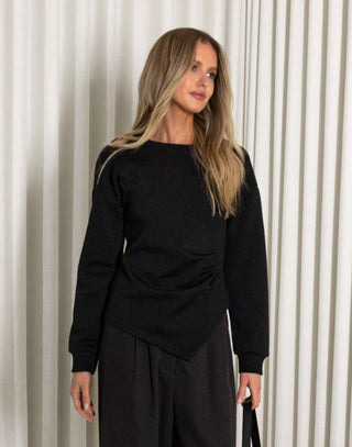 Woman in a black outfit standing against a white curtain