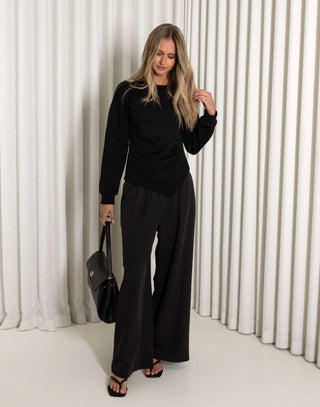 Woman in a black outfit standing against a white curtain