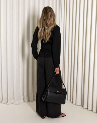 Woman in a black outfit standing against a white curtain