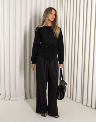 Woman in a black outfit standing against a white curtain