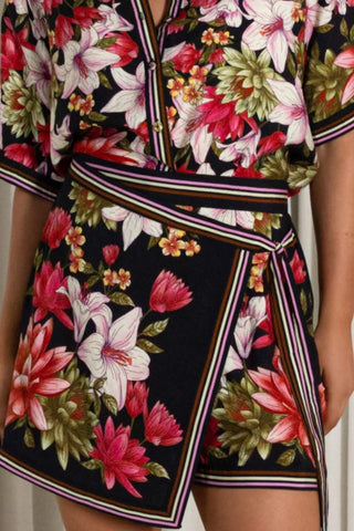 Close-up of a floral wrap-style romper or dress with a black base and large pink, white, and green flowers, plus striped trim details.