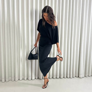 Woman in a black outfit posing against a white curtain