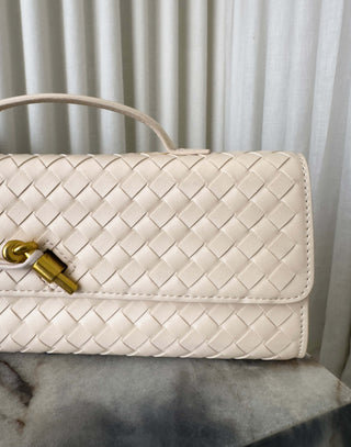 Cream woven handbag with gold clasp on a marble surface