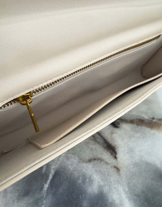 Close-up of a cream handbag with a gold zipper on a marble surface