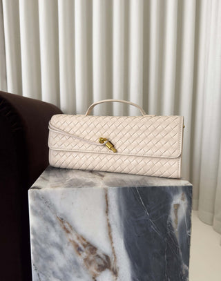 Cream-colored handbag with a gold lock on a marble surface with a curtain background