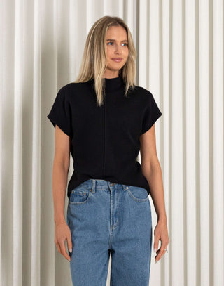 Woman wearing a black top and blue jeans against a neutral background