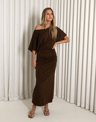 Woman wearing a brown off-shoulder dress against a white curtain background