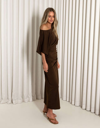Woman wearing a brown off-shoulder dress against a white curtain background