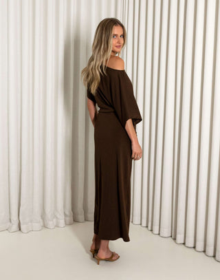 Woman wearing a brown off-shoulder dress against a white curtain background