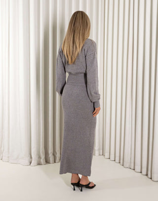 Woman wearing a gray knit outfit standing against a white curtain background