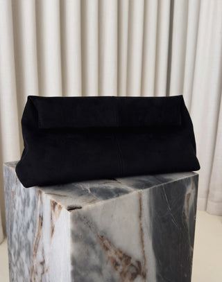 Black clutch bag on a marble block with a neutral background