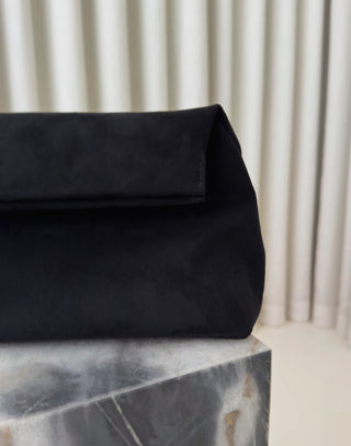 Black clutch bag on a marble surface with a neutral background