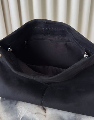 Close-up of a black leather bag with zippers on a marble surface.