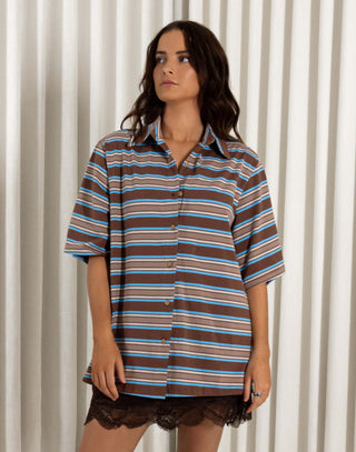 Woman wearing a striped shirt and lace shorts standing against a white curtain. Stripe button down cotton top with collared neckline and relaxed fit