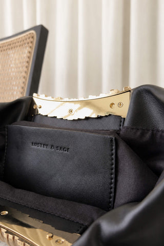 Close-up of a black leather handbag interior with a black fabric pocket embossed with 'LUSTRE & SAGE' and gold-tone hardware.