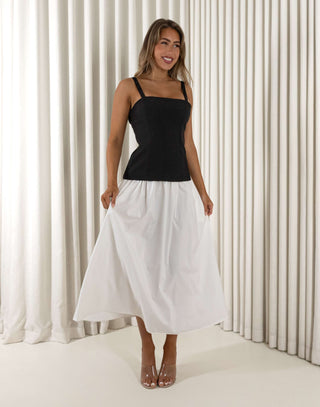 Woman wearing a black top and white skirt standing against a white curtain. Amanda black and white two-tone midi dress with square neckline
