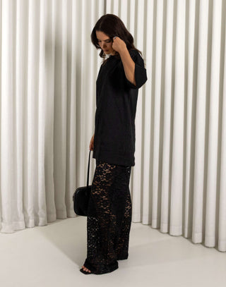 Woman wearing a black oversized t-shirt and black lace pants against a striped background Black longline cotton t-shirt with relaxed fit