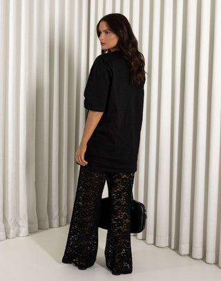Woman wearing a black oversized t-shirt and black lace pants against a striped background Black longline cotton t-shirt with relaxed fit