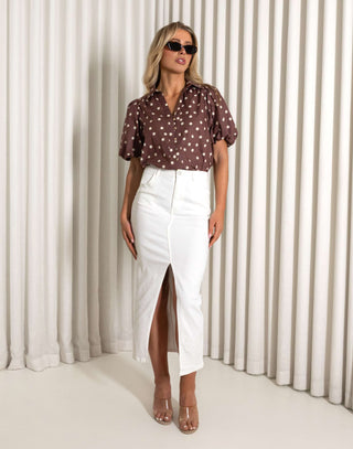 Woman wearing a brown polka dot blouse and white skirt against a white curtain background Brown polka dot cotton shirt with short sleeves and relaxed fit