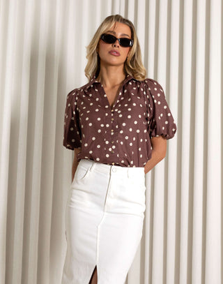 Woman wearing a brown polka dot blouse and white skirt against a white curtain background Brown polka dot cotton shirt with short sleeves and relaxed fit