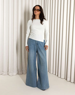 Woman white top, and blue jeans against a neutral background high waisted wide leg jeans in blue