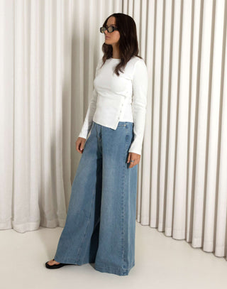 Woman wearing a white top, and blue jeans against a neutral background high waisted wide leg jeans in blue