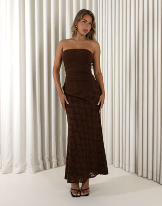 Woman wearing a brown strapless dress against a white curtain background