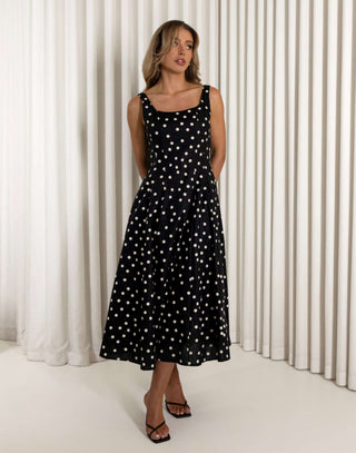 Woman wearing a black dress with white polka dots against a white curtain background Christine black A-line 100% cotton dress