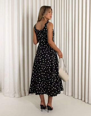 Woman wearing a black dress with white polka dots against a white curtain background Christine black A-line 100% cotton dress