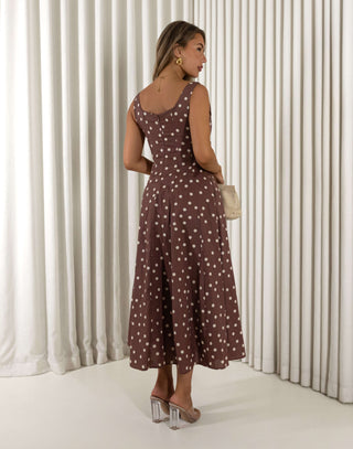 Woman wearing a brown dress with white polka dots in front of white curtains. Christine A-line midi dress in polka dots with squoval neckline
