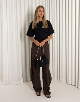 Woman wearing a black top and brown striped pants against a white curtain background