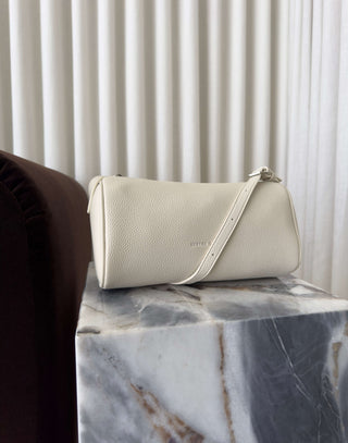 Beige handbag on a marble surface with a white curtain background Danes ivory shoulder bag with adjustable strap