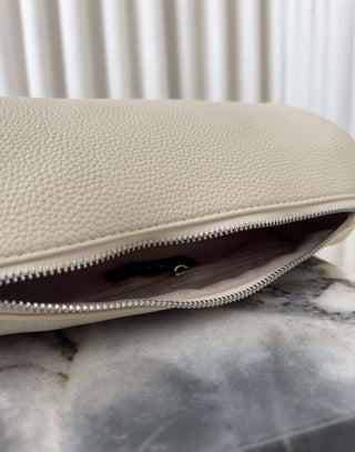 Beige clutch bag with a zipper on a marble surface Danes ivory shoulder bag with adjustable strap