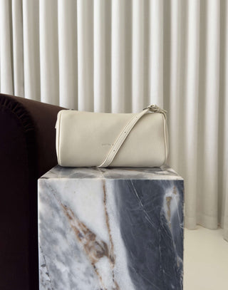 Beige handbag on a marble surface with a neutral background Danes ivory shoulder bag with adjustable strap