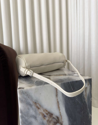 Beige handbag with a white strap on a marble surface with curtains in the background Danes ivory shoulder bag with adjustable strap